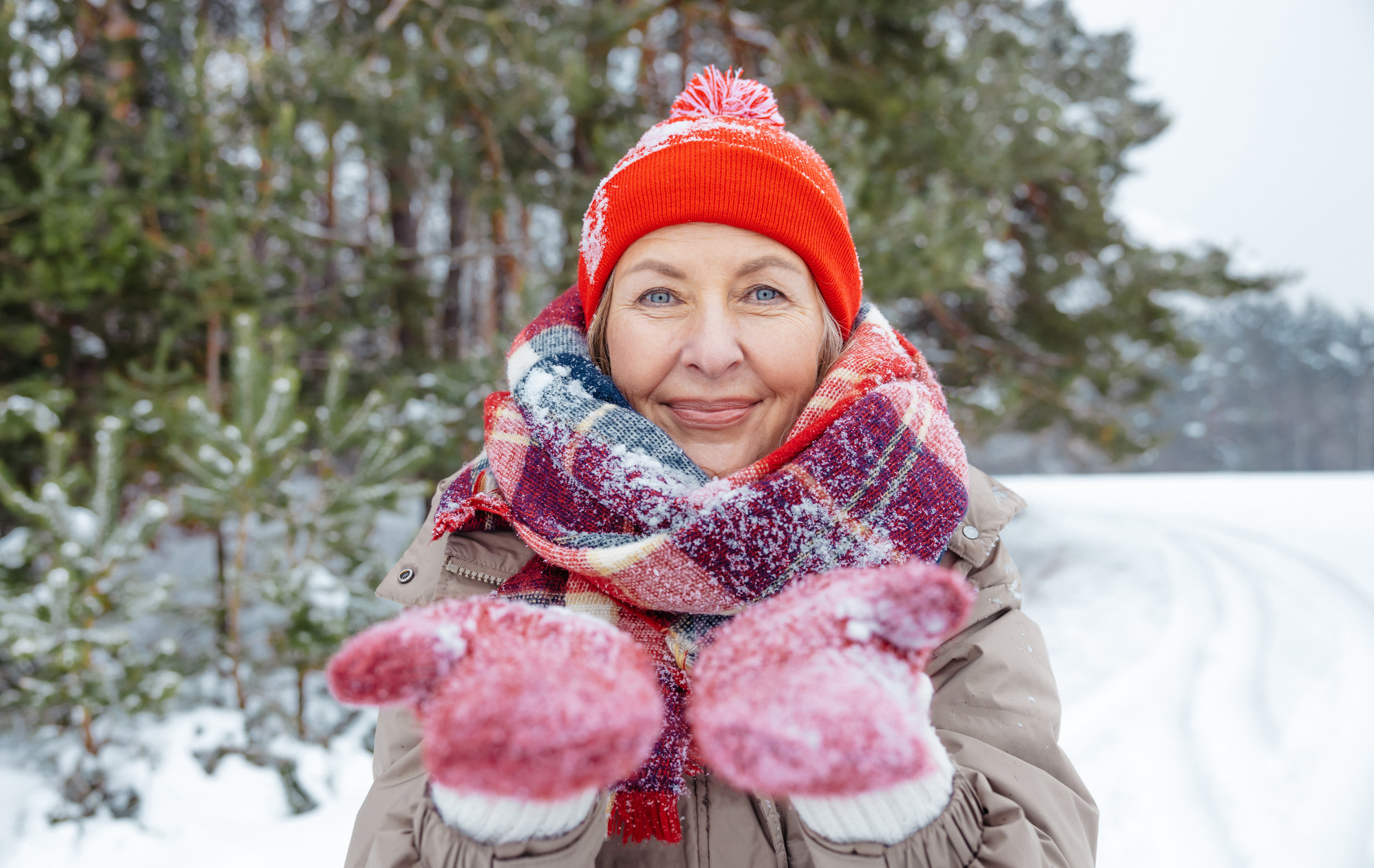 Kvinne med votter og lue ser mot kamera