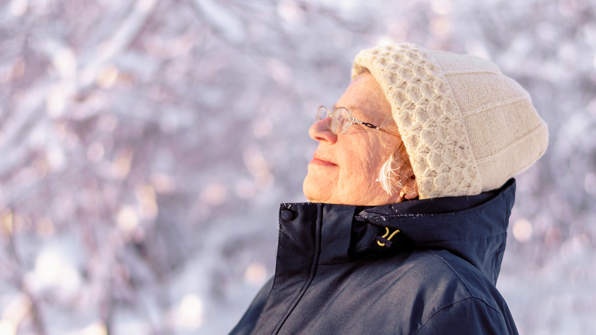Kvinne i hvit lue myser mot solen i vintervær