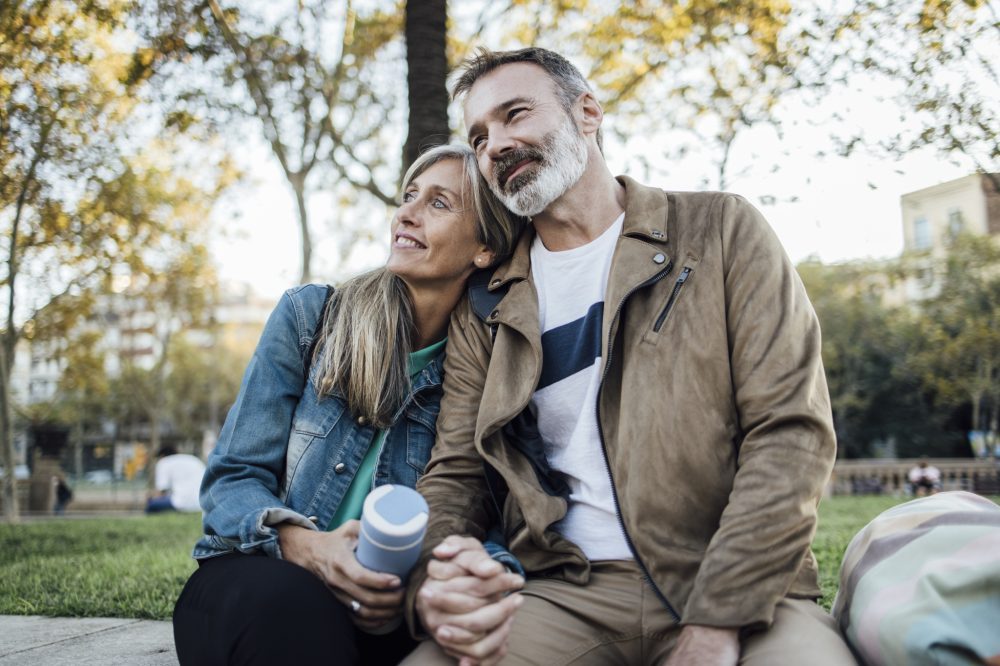 Par sitter på en benk i en park og holder hender og drikker kaffe