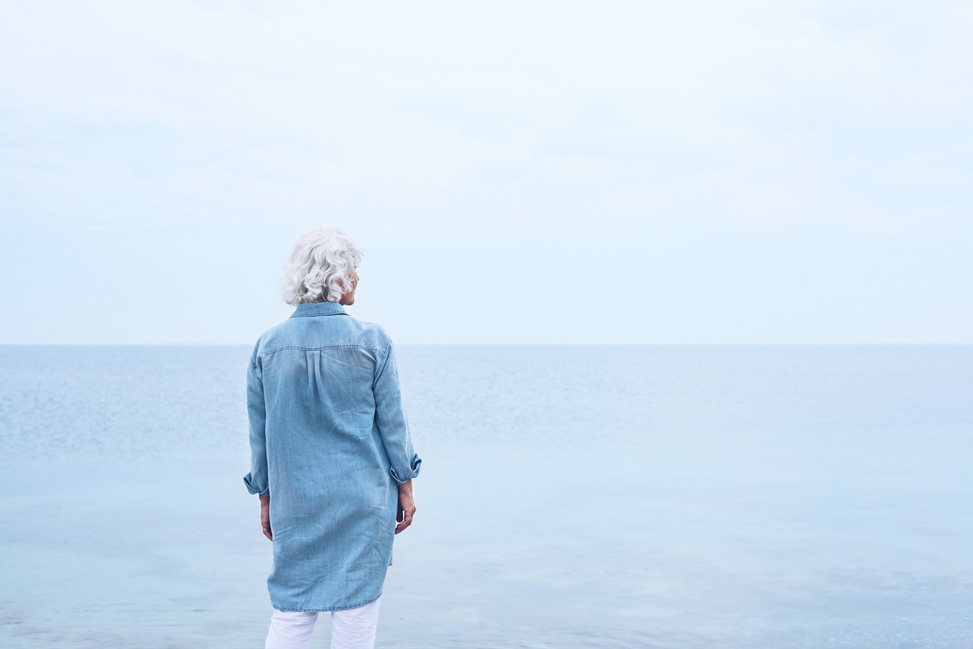 Kvinne står med ryggen til og ser ut over havet