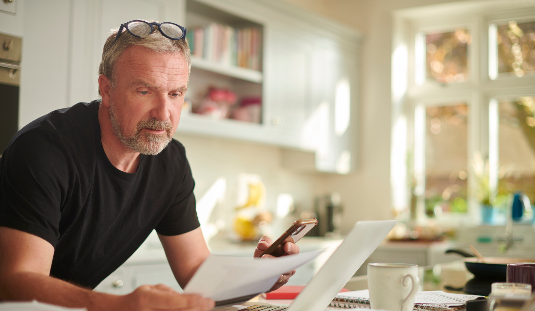 Godt voksen mann med brillene på hodet holder papirer og ser frustert ut foran en PC skjerm