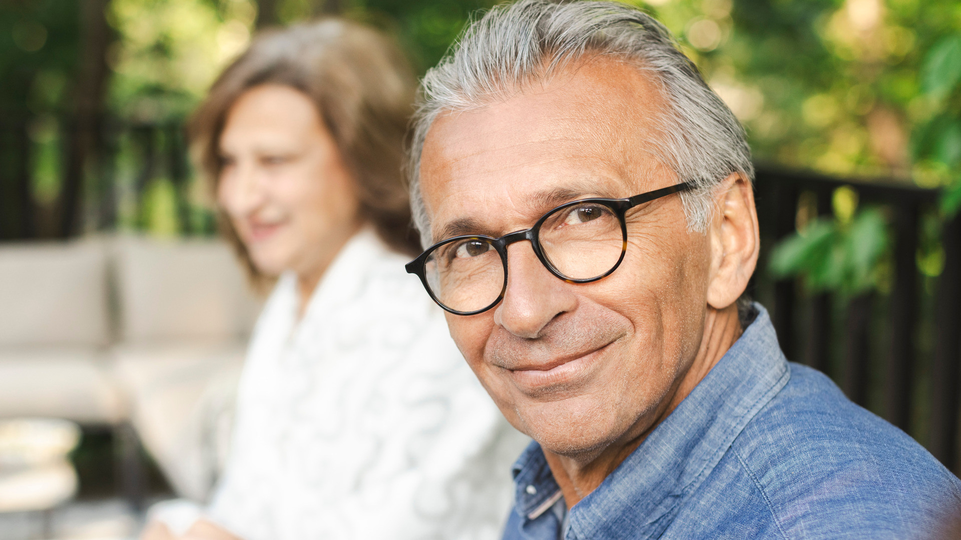 Eldre mann sitter i et hageselskap og ser smilende mot kamera